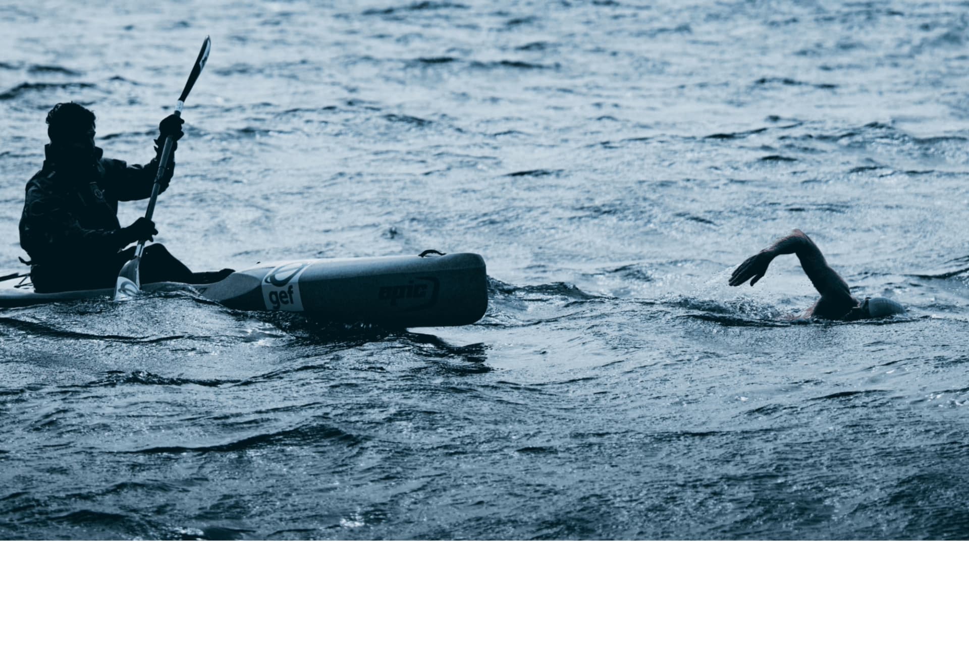 An escort kayaker paddling alongside a swimmer during an open water session