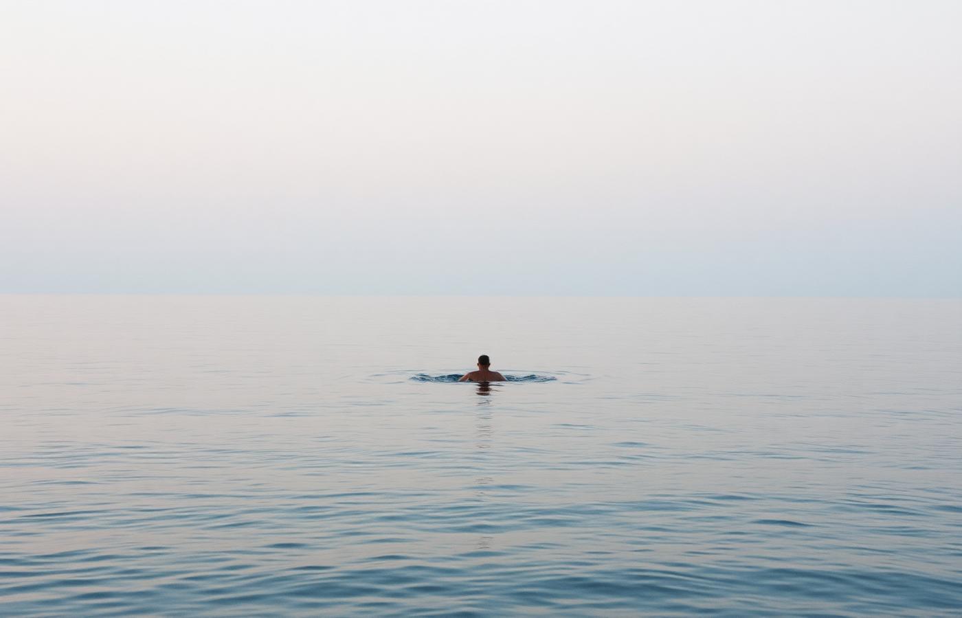 A single swimmer in calm open water at dawn
